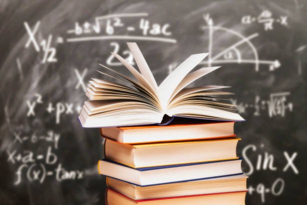 opened book on a stack in front of a blackboard with mathematical formulas